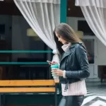 Woman looking at phone while holding cup making $47,000 a year.