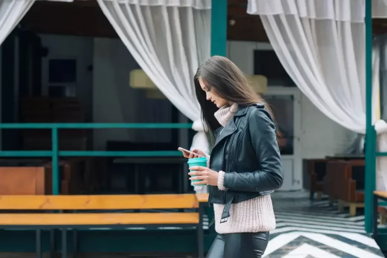 Woman looking at phone while holding cup making $47,000 a year.
