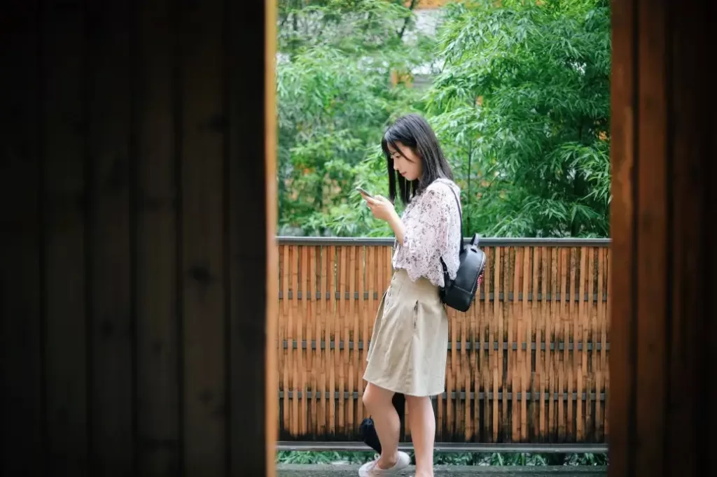 Woman holding her phone while wearing a backpack making $48,000 a year.