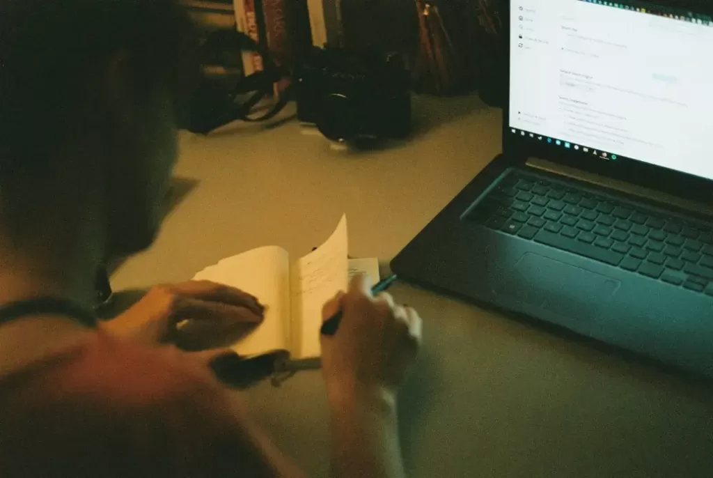 Person writing in a notebook next to a computer earning $94,000 a year.