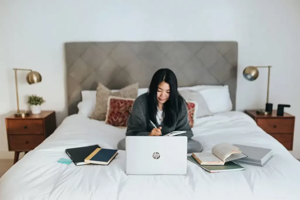 Woman sitting on a bed working on a laptop earning $99,000 a year.